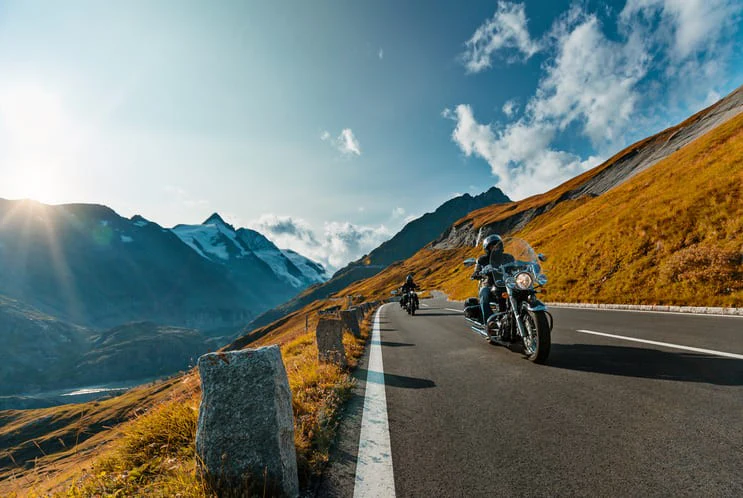 Motorcycle riders on a scenic road trip through the Alps with mountains and sunny sky background.