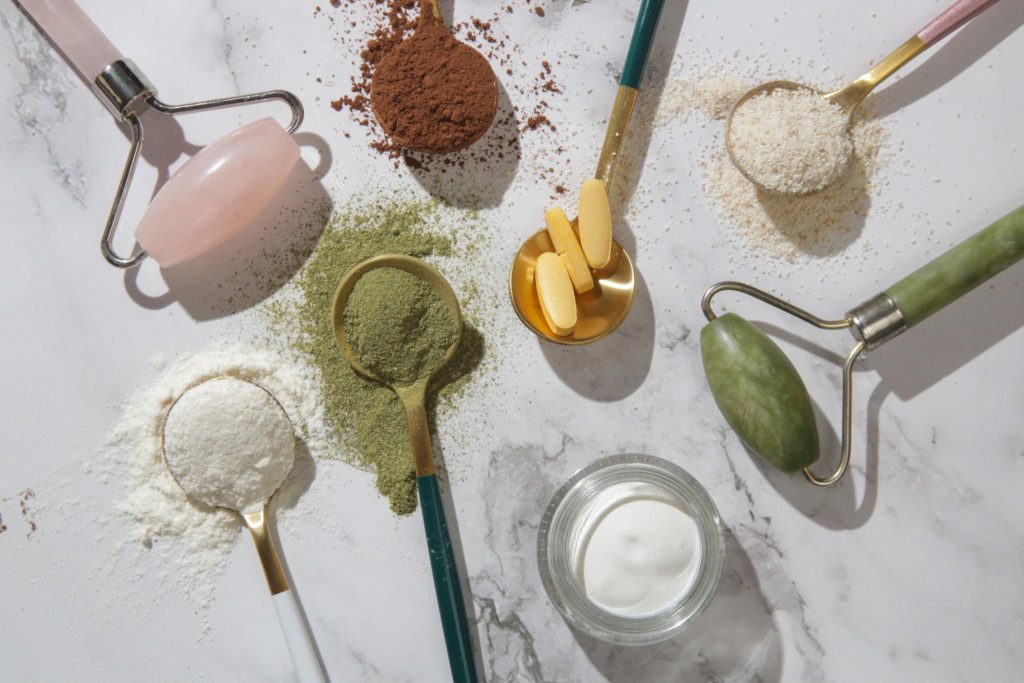 Assorted superfood powders and collagen peptides with jade rollers, illustrating Ancient Nutrition benefits for anti-aging and skin beauty